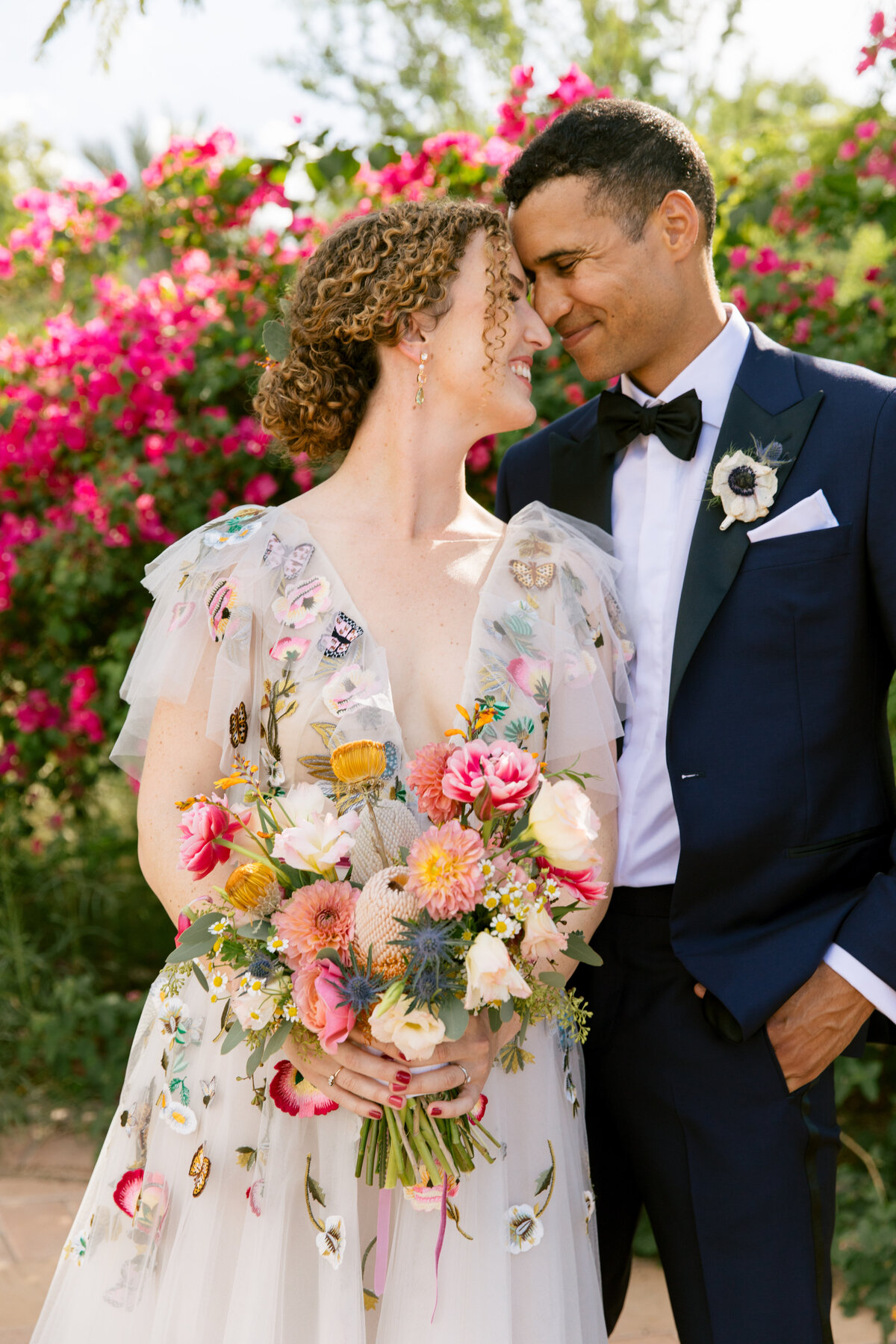 Bride and groom nuzzle noses on their wedding day. The bride is holding a colorful wedding bouquet and she is wearing a colorful appliques floral Claire Pettibone wedding dress.