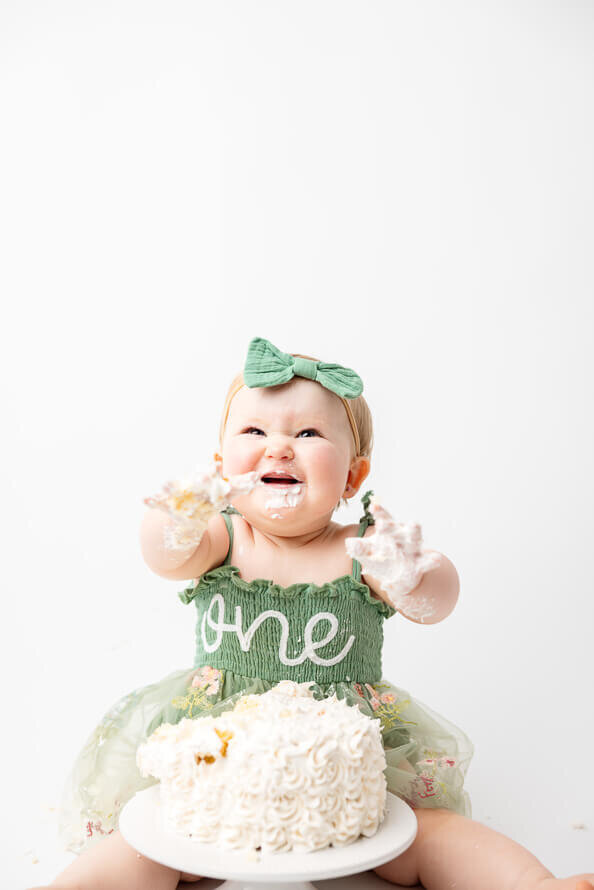 Baby laughs while holding up messy hands during her cake smash photo session.
