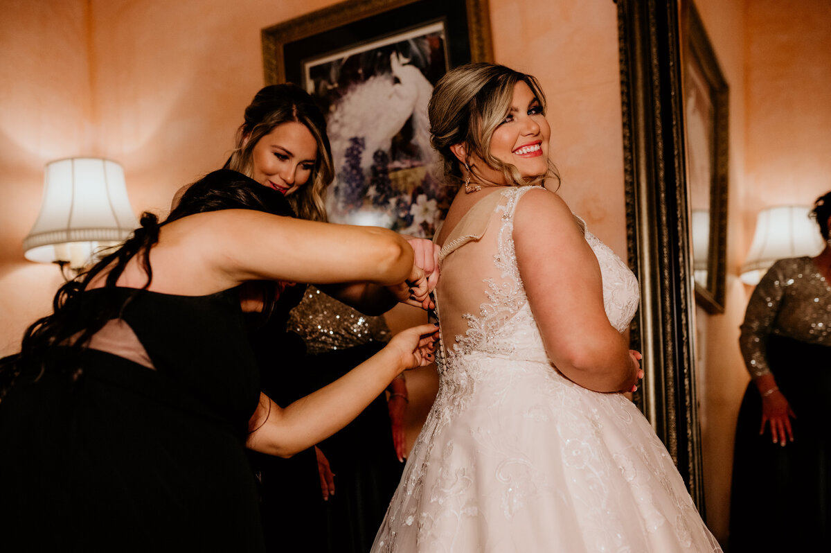 bridesmaids helping the bride into her dress in the bridal suite photographed by Little Rock wedding photographer