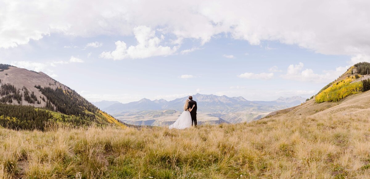 Bride and groom standing together on a high mountain overlook with panoramic views of Telluride, Colorado.