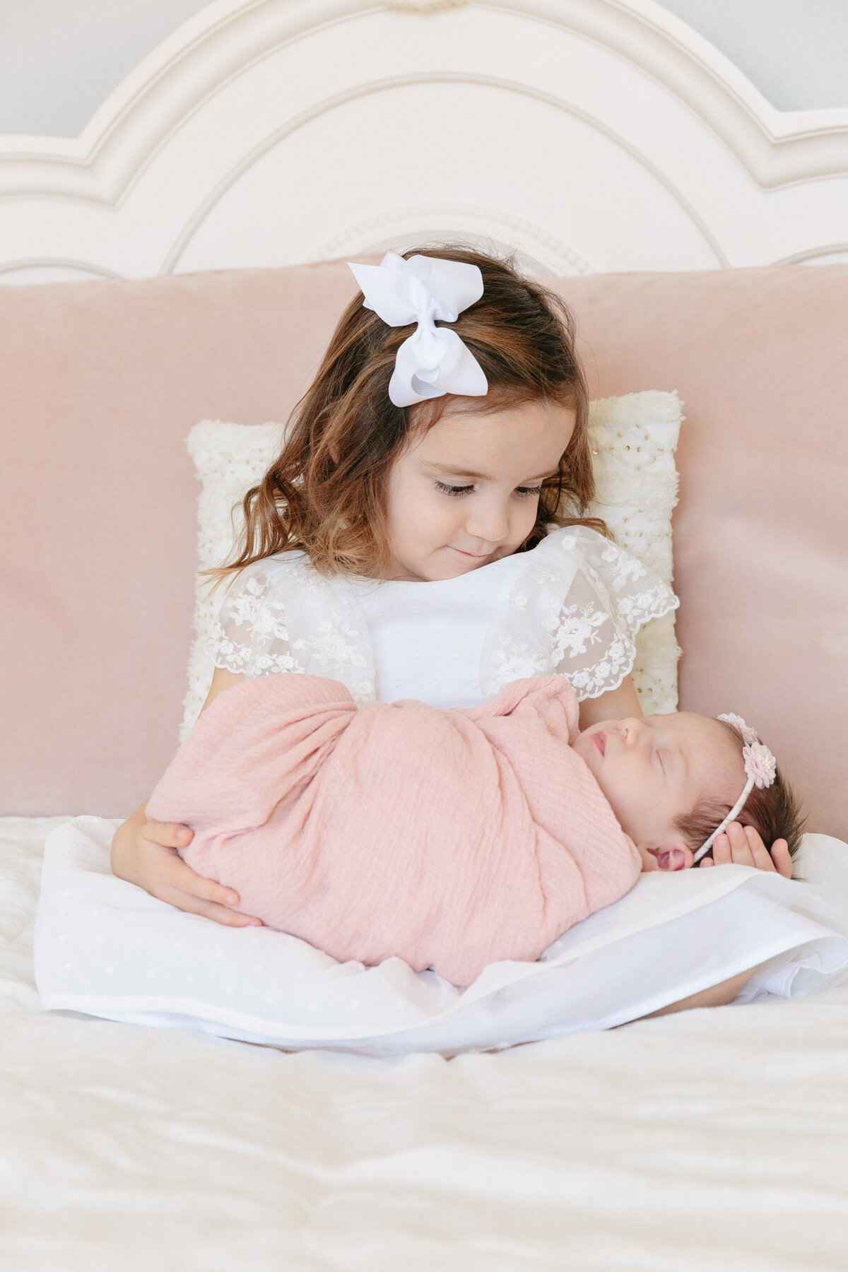 A small girl sitting on a bed holding a baby