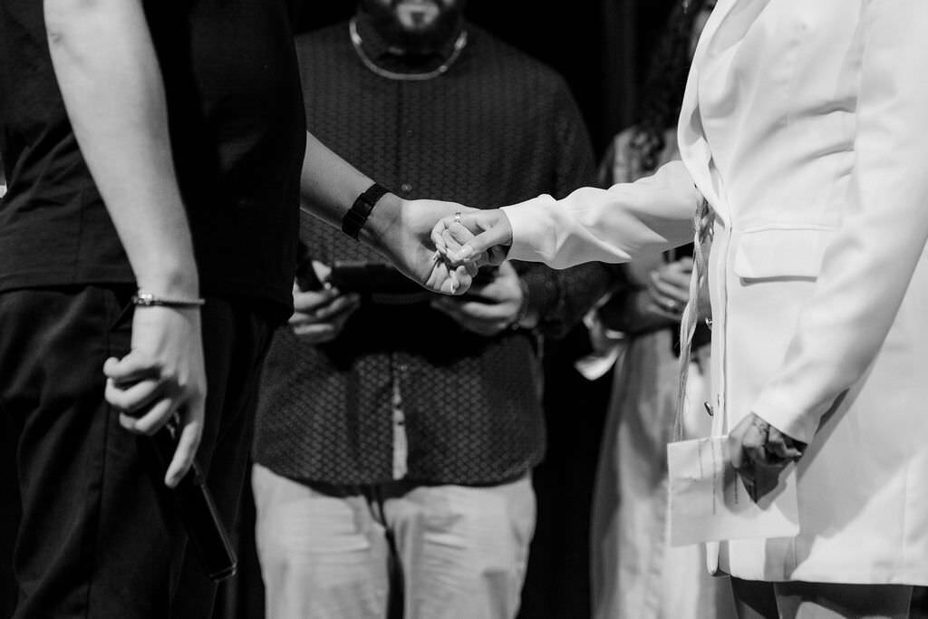 black and white photo of bride and groom holding hands and officiant behind them