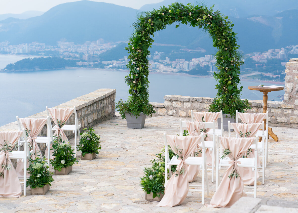 A decorated wedding arch of greenery frames the ceremony aisle at a destination wedding overlooking the ocean in