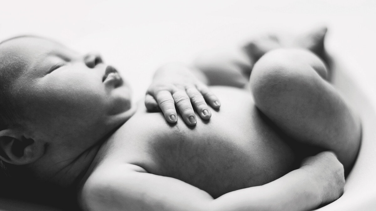 newborn baby photographed on her back, wth a macro camera to capture the details of her tiny hands, shown inblack and while