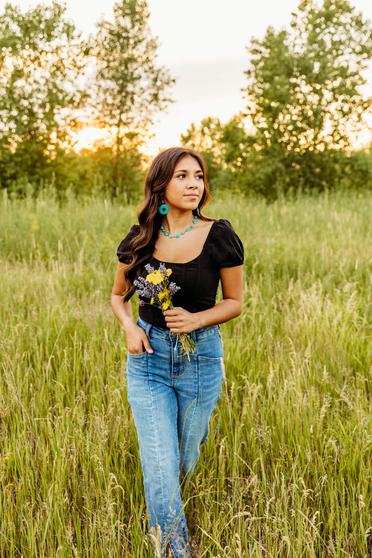 girl walking through a grassy field while holding a bouquet of wildflowers.