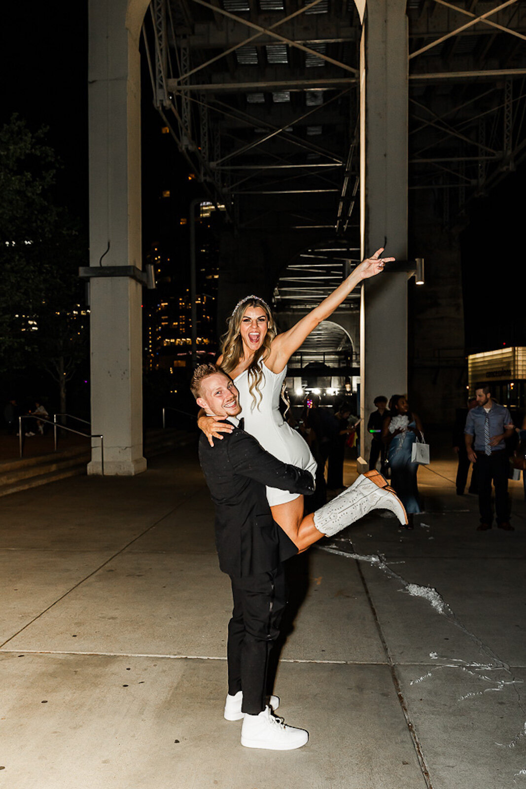 Groom lifting his bride in the air as she makes a peace sign with her fingers