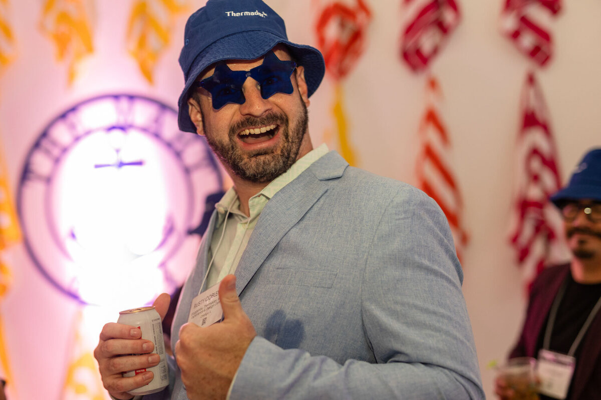 Man in blue hat and star glasses smiles and poses at event