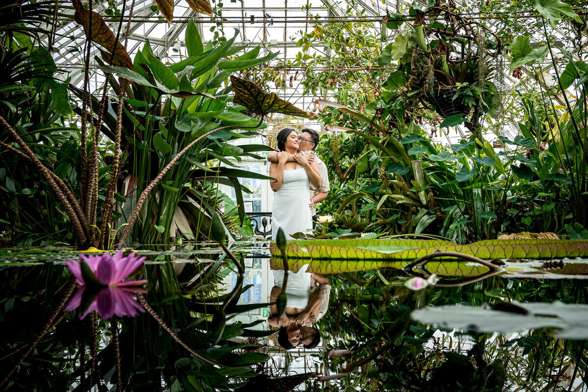 A loving couple embraces inside the Conservatory of Flowers in Golden Gate Park, surrounded by lush greenery and soft natural light, creating a dreamy and intimate moment.