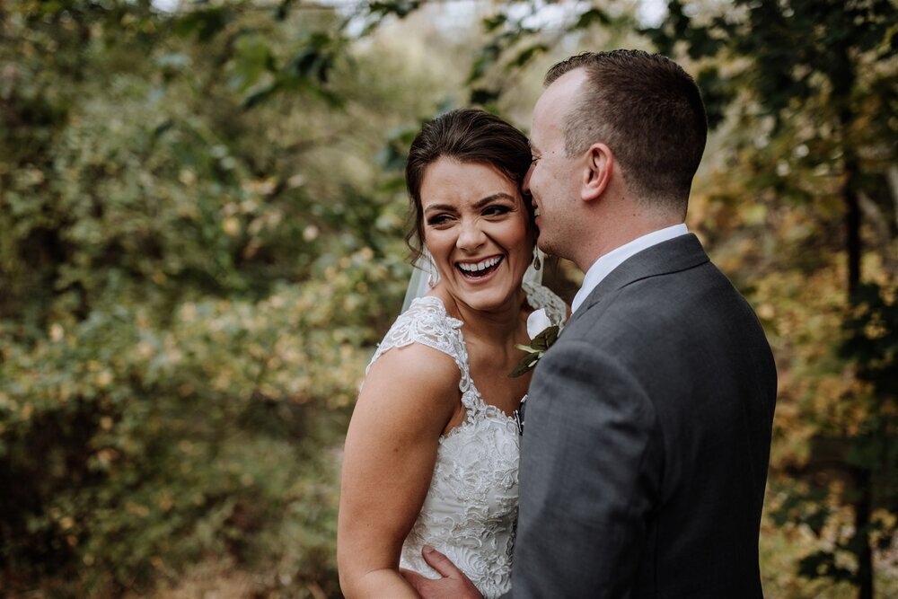 Bride and groom holding hands looking at each other while standing in front of rolling hills with the sunlight coming down on them