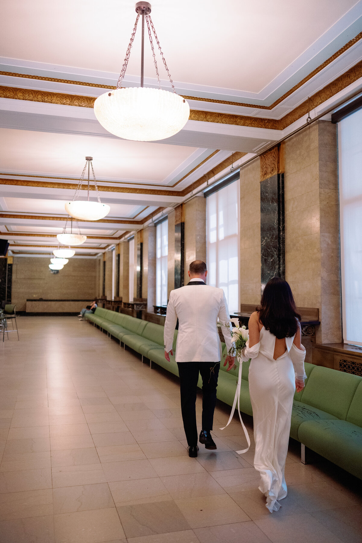 Bride and groom walking hand in hand through the grand hallway of New York City Hall, captured during Japna and Chris’s intimate elopement by NYC wedding photographer Perry Hancock.