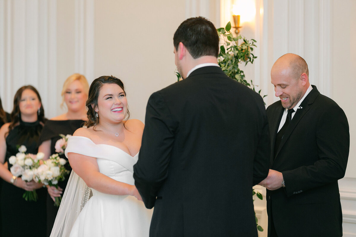 bride laughing and looking at the groom during their ceremony in the Governor’s Room at The Adolphus in Dallas, capturing a joyful and heartfelt wedding moment.