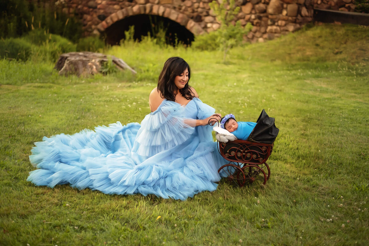 Gorgeous mom in blue luxury ruffle gown at outdoor by Greater Toronto Newborn Photographer at Vineland Research and Innovation centre holding her baby girl in a carriage.