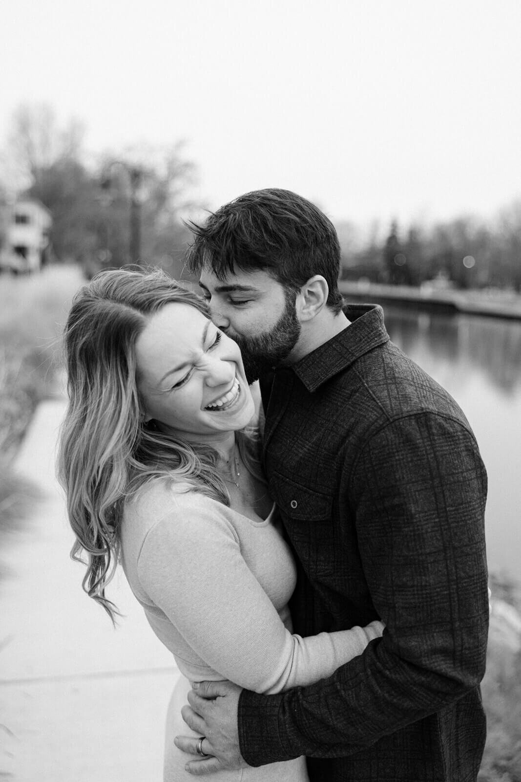 Man kissing woman beside a lake at  maternity photos in Finger Lakes New York