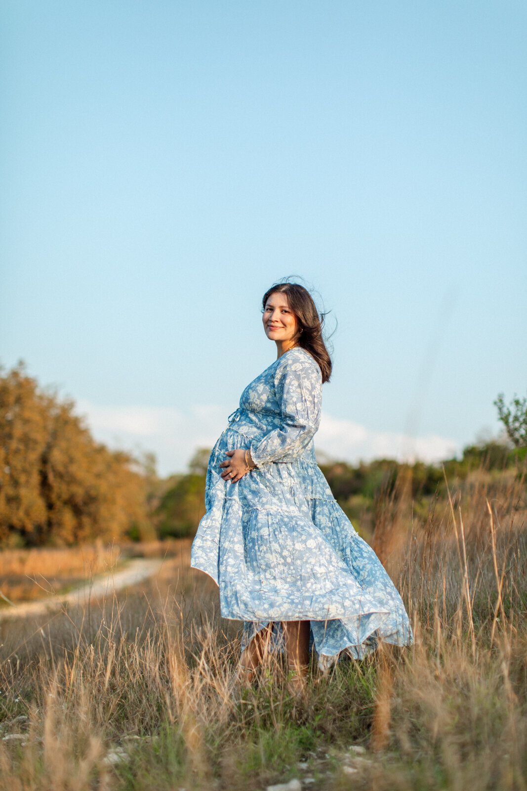 Maternity portrait of a pregnant woman wearing a blue dress in a field, photographed by San Antonio family photographer Sara James.