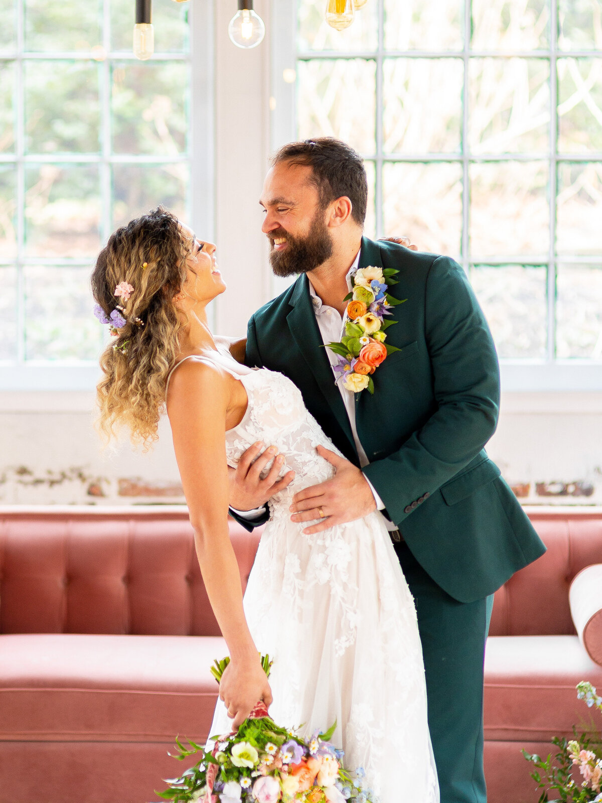 Bride and groom smiling while hugging in front of pink velvet couch