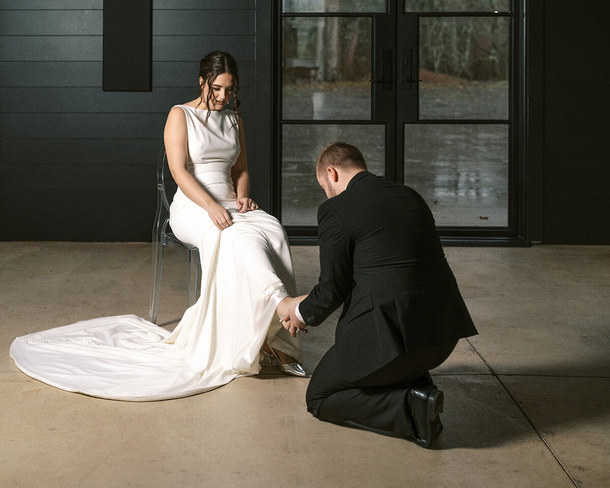 A bride sits in a chair while the groom helps put on her shoe during a styled photo shoot at Sage & Social.