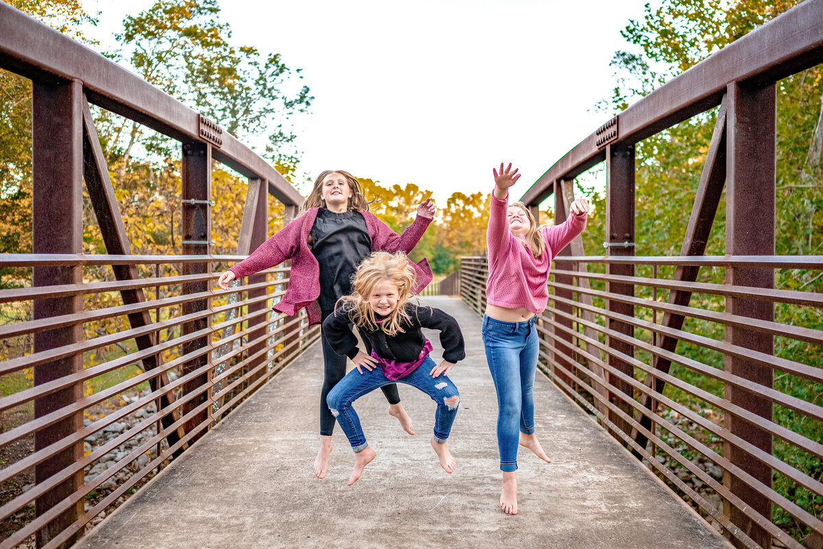 Three sister jump on a bridge during family photos at Hayes Nature Preserve