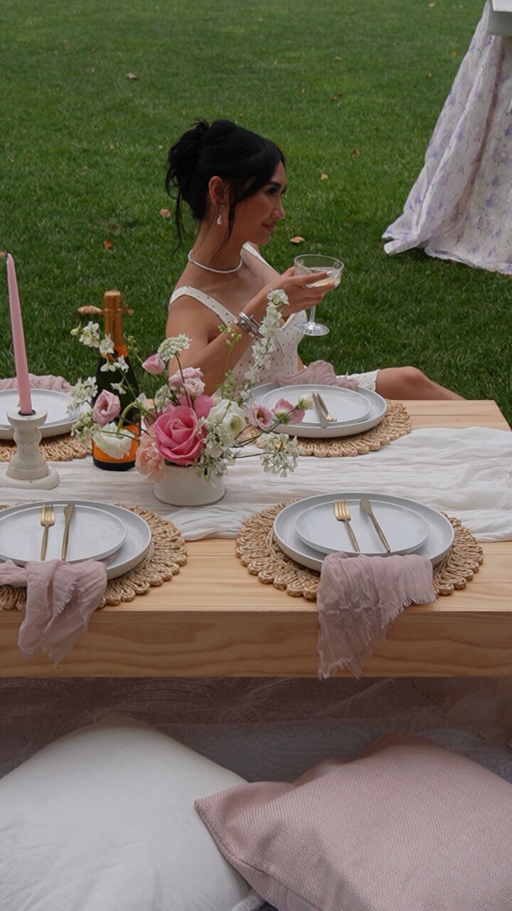 Styled picnic table with woven placemats, blush napkins, florals, and champagne, designed by Yours Truly, a wedding planner and designer in New Jersey.