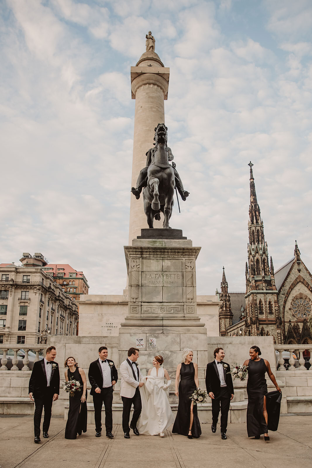 Newlyweds and their wedding party standing in front of a statue 
