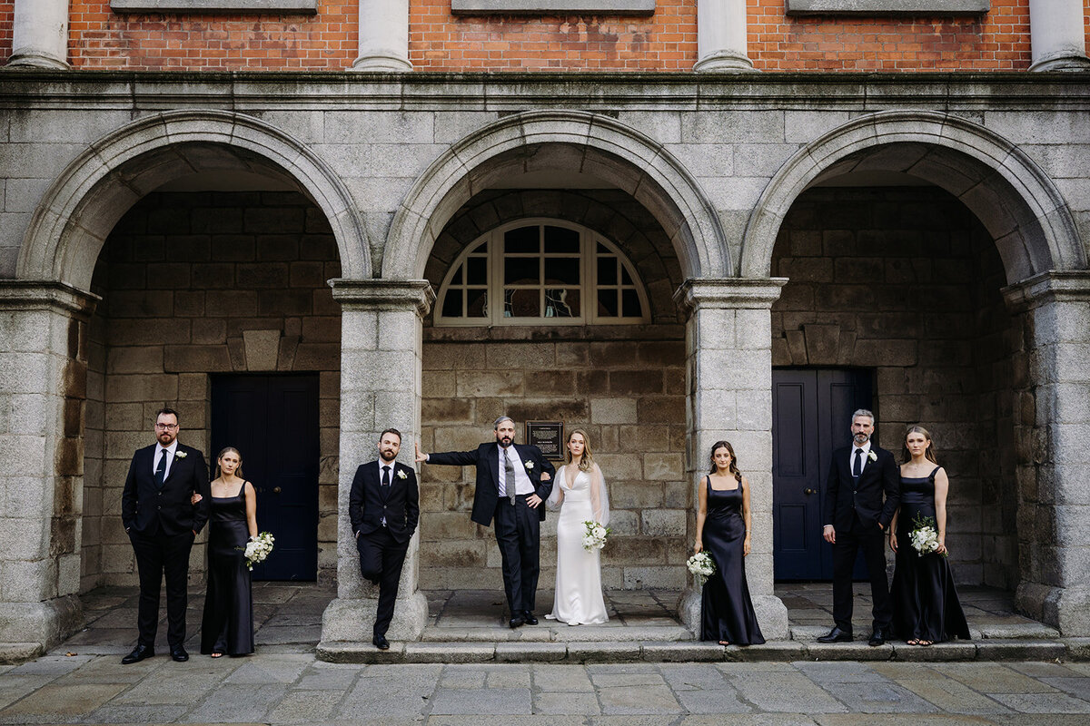 Bride and groom with their wedding party leaning against archways at Smock Alley in Dublin, Ireland