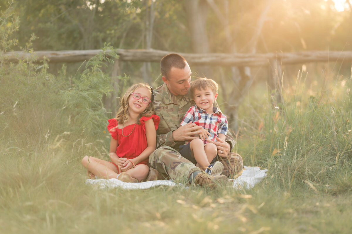Military dad in uniform snuggles his kids at Hardberger Park in golden sunrays.