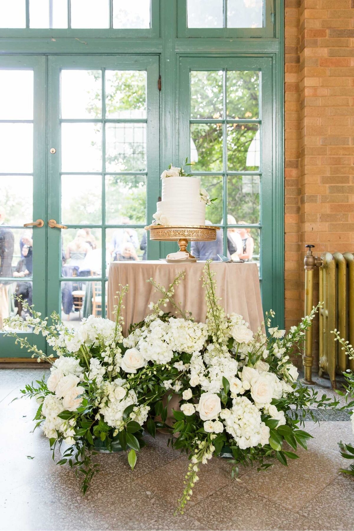 Cake table with lush floral encircling with white and green florals at Columbus Park Refectory at a Luxury Chicago Outdoor Historic Wedding Venue.