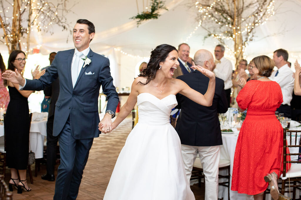A very happy and excited bride holding the hand of her new husband and walking in to the reception party.