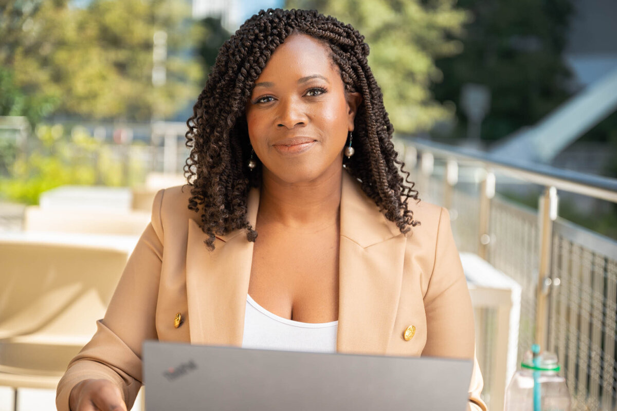 A portrait of a professional woman working outdoor on her laptop and looking smiling to the camera