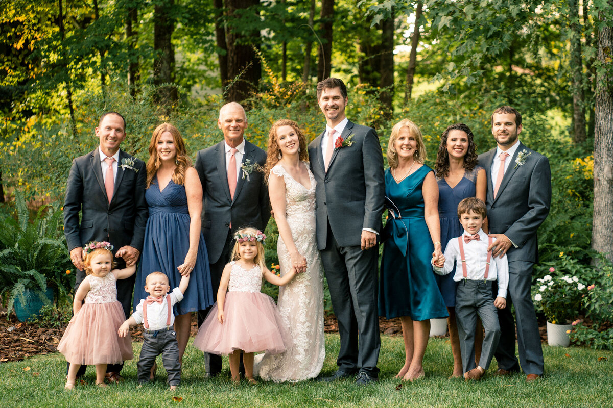 A happy, multi-generational family portrait at a wedding, with everyone dressed in formal attire and smiling in an outdoor setting
