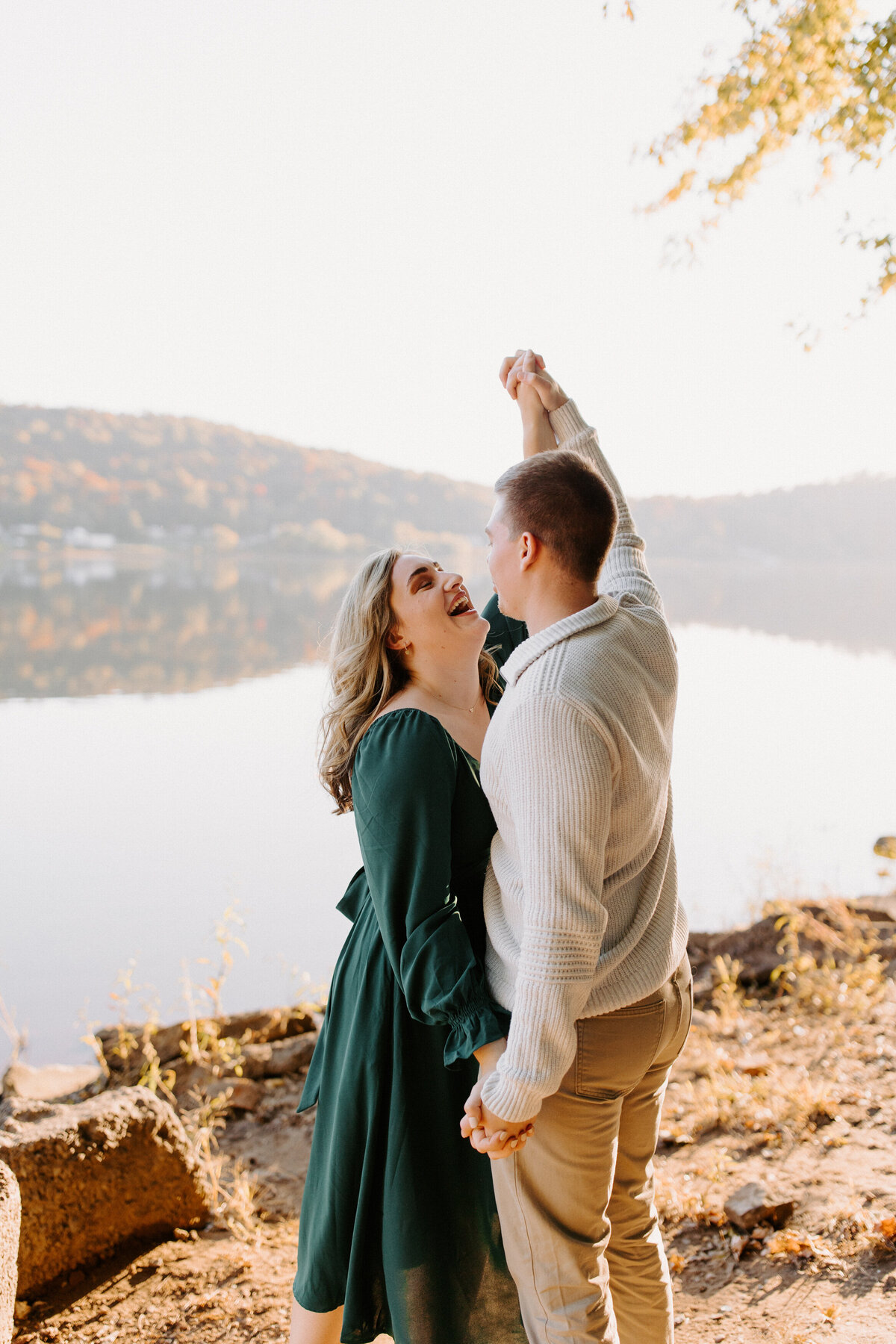 couple standing by a lake and smiling while holding their hands up