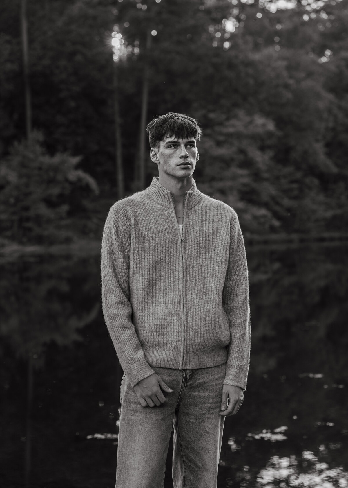 Black and white editorial portrait of a man standing by a still lake—minimalist styling with cinematic, introspective mood.