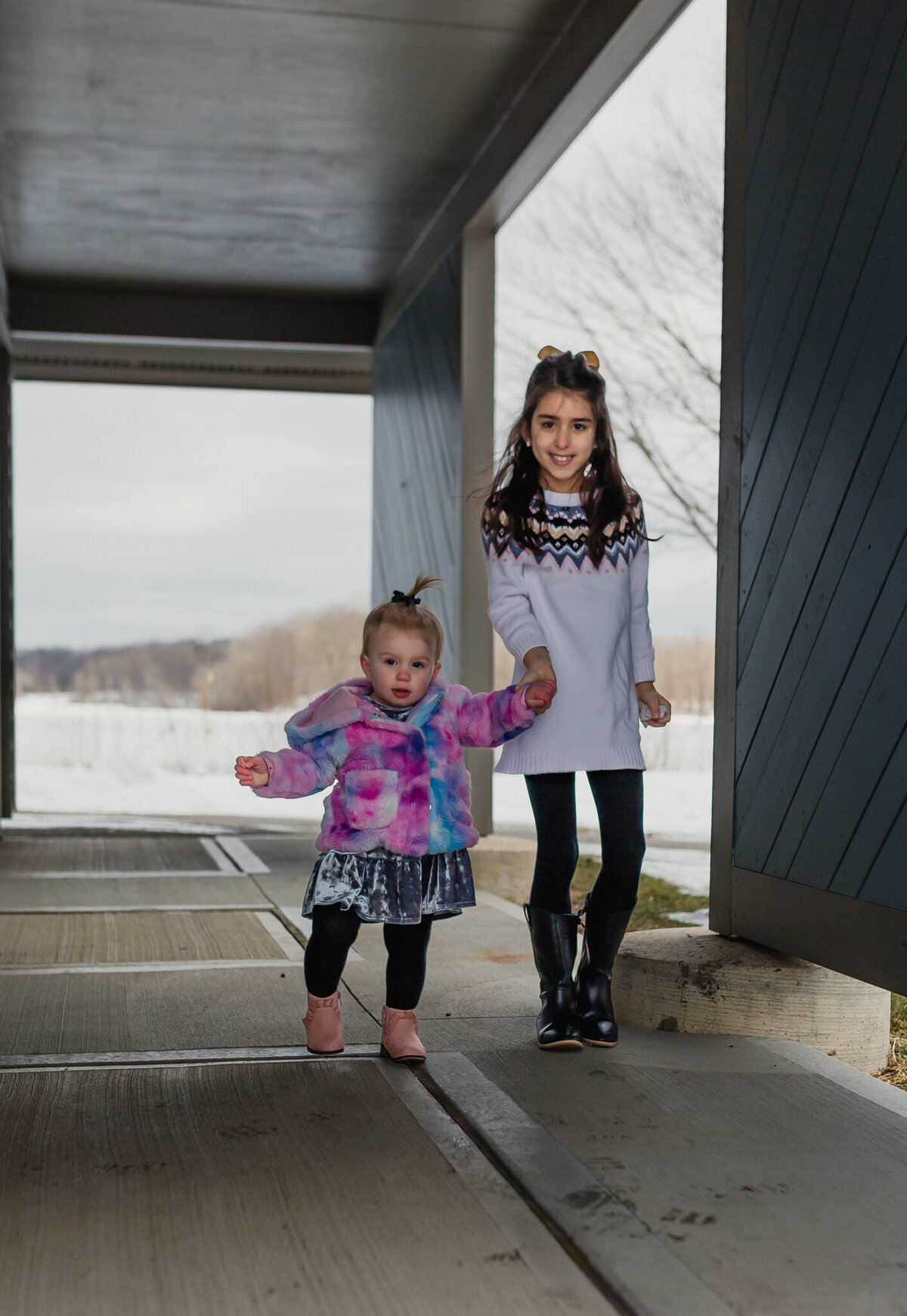 Two young children walk  outside holding hands.