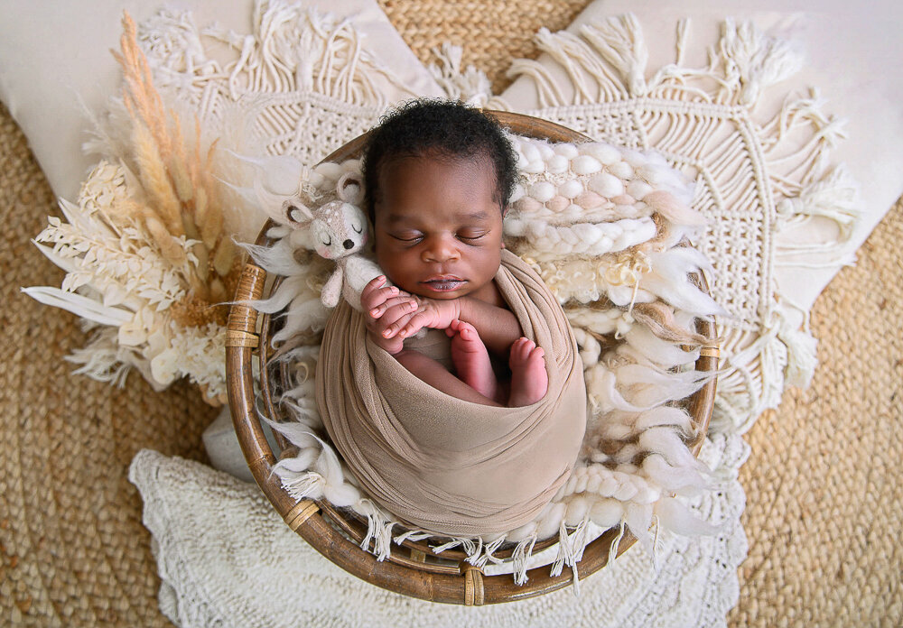 Black newborn baby boy wrapped in beige for her newborn photography session