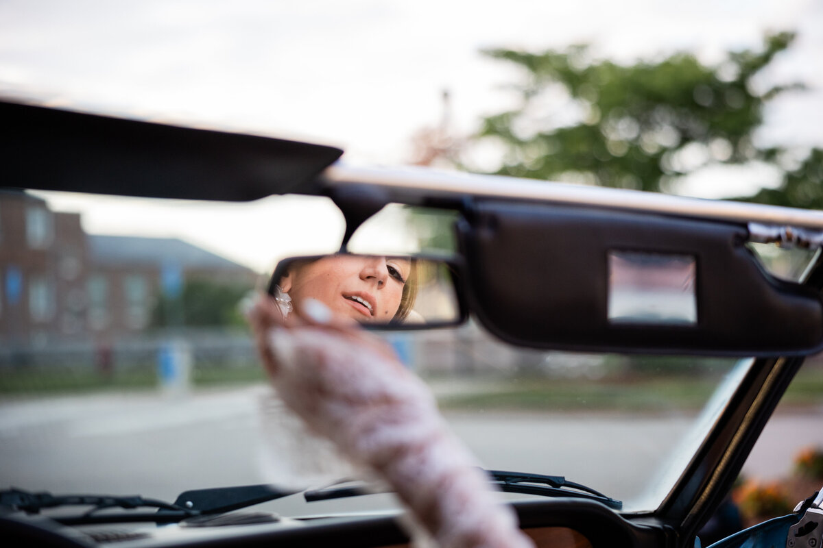 A Photograph of a bride looking in the rear view mirror of a classic car.