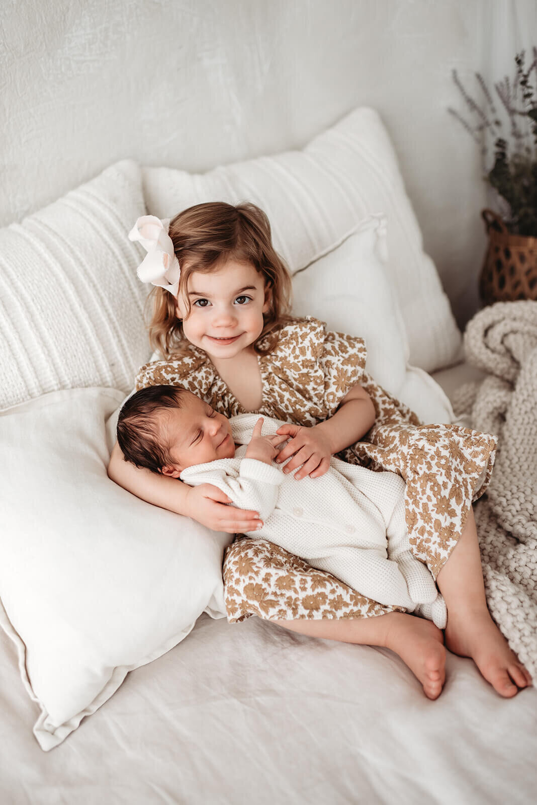 little girl leaning agains pillows holding her newborn brother