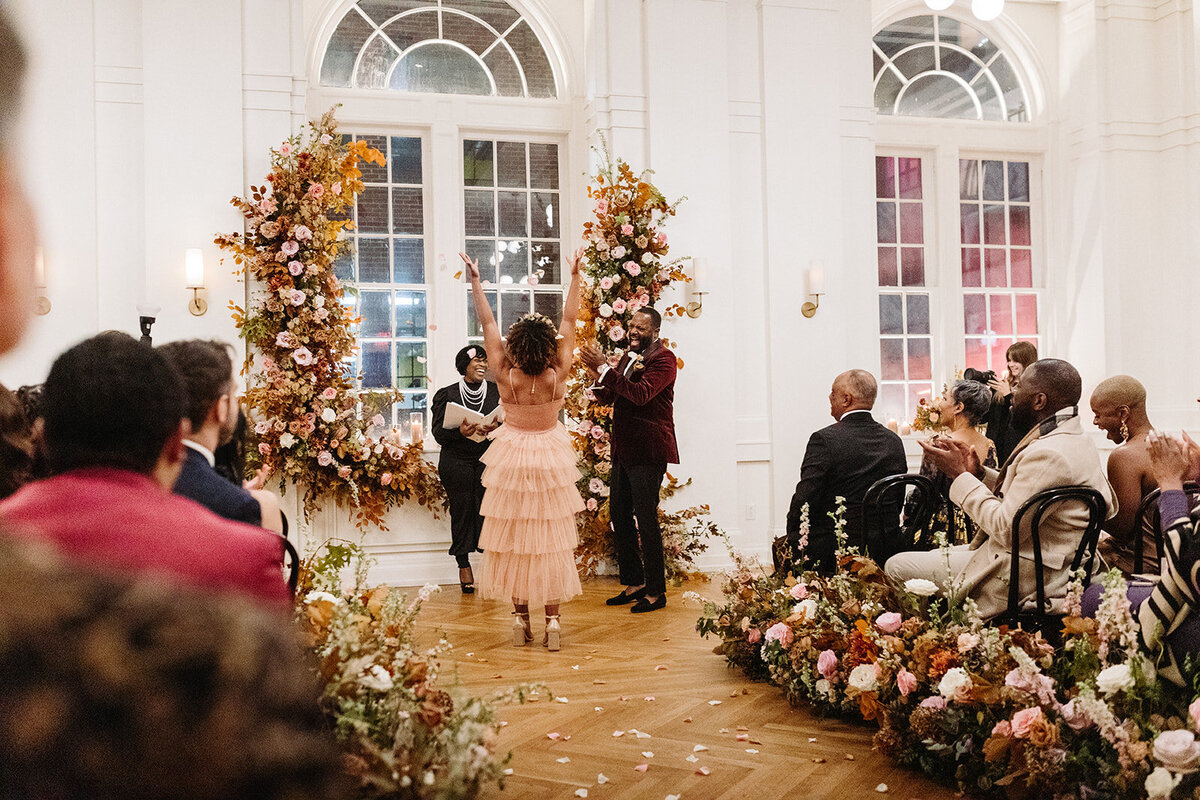 Artful asymmetrical floral wedding ceremony backdrop sets the autumnal hues of mauve, dusty rose, burgundy, terra cotta, and copper florals composed of roses, copper beech, delphinium, raintree pods, mums, and fall foliage. Design by Rosemary and Finch in Nashville, TN.