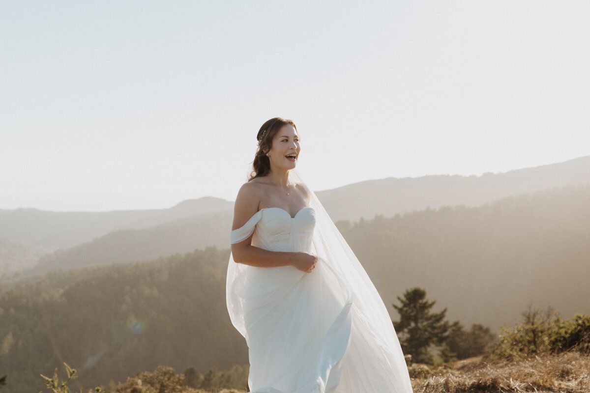 Bride laughing while sanding on top of mountain at golden hour