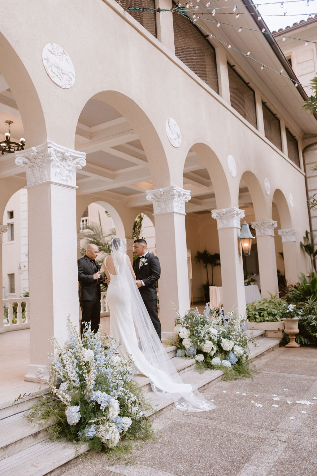 bride and groom during ceremony standing under arches at cafe julia with white and blue flowers surrounding them