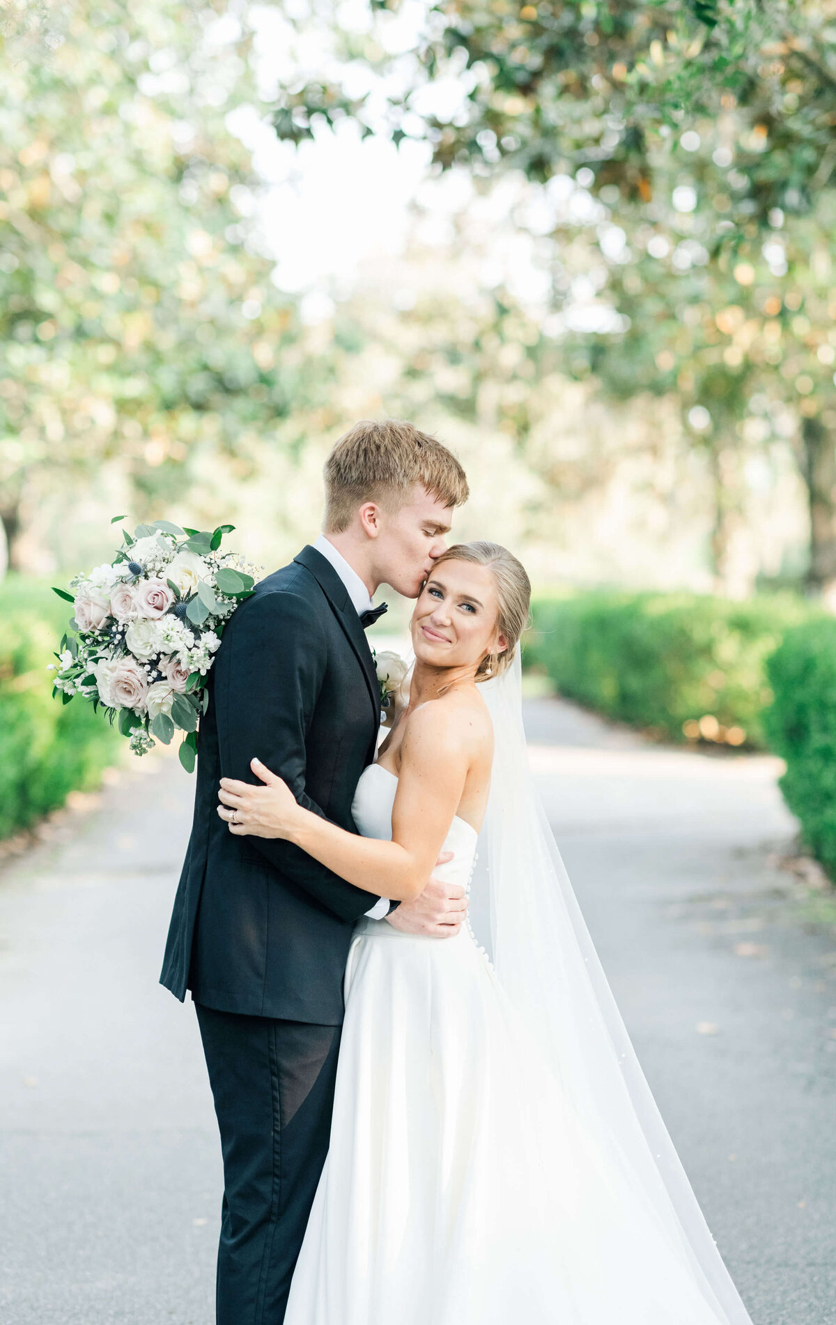 Alabama wedding couple standing in a garden walkway with groom kissing brides forehead as she looks at the camera for bridal portraits