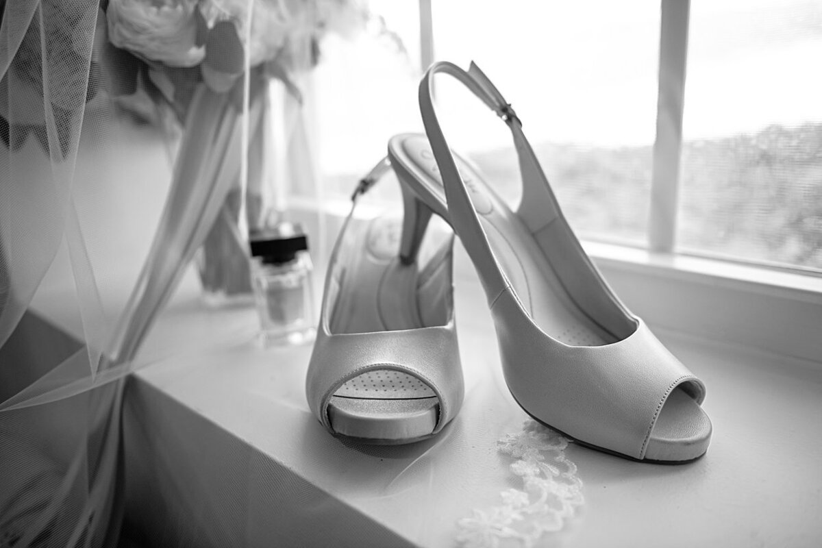 Black and white image of peep-toe heels, perfume, veil and bouquet in vase