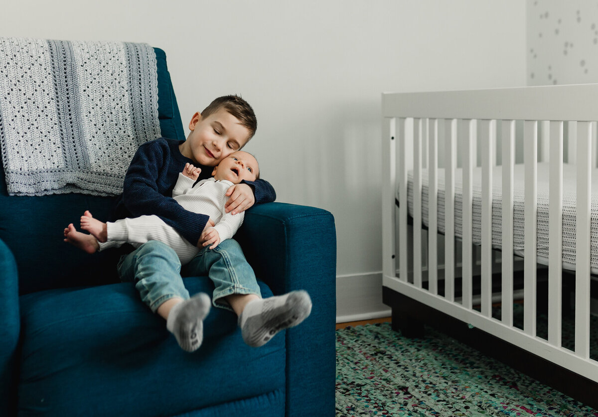 Young child holding newborn baby sitting in a chair.