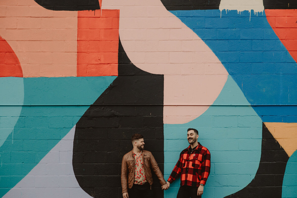 A couple holding hands in front of a mural 