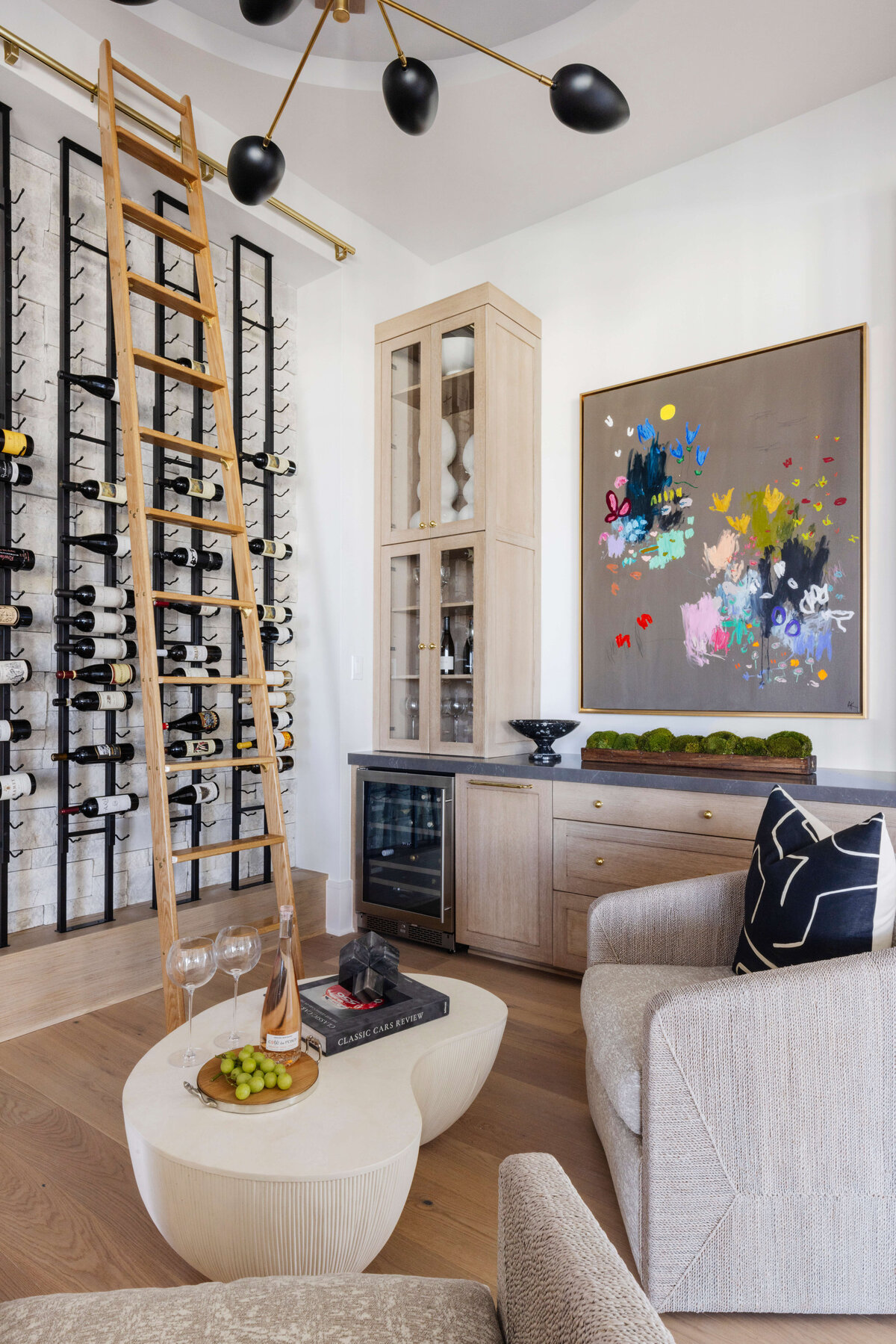 oyster creek studios hughes wall of wine and wooden ladder with gray armchairs and white coffe table with modern artwork