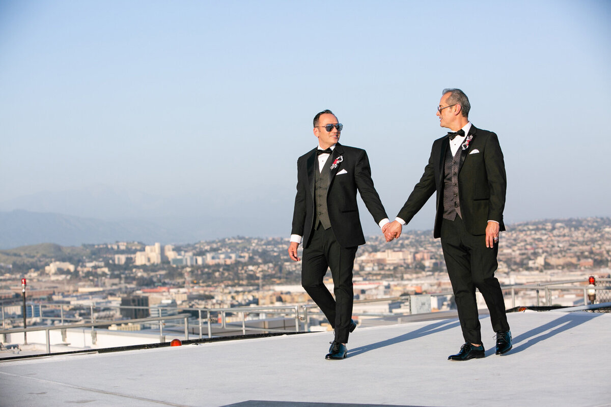 Two grooms holding hands and walking on a rooftop