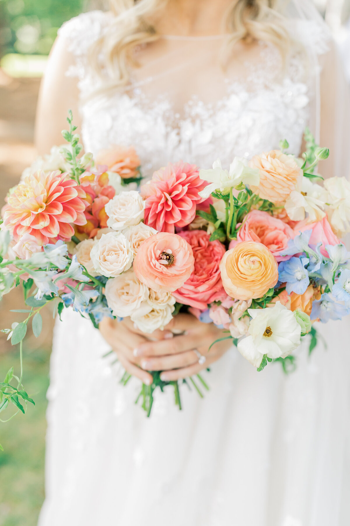 A bride in a lace wedding dress holds a bouquet of vibrant garden roses, peonies, and delicate wildflowers
