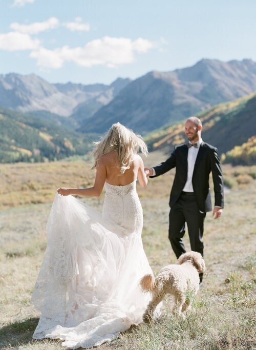 fine+art+photo+of+bride+and+groom+running+through+field+in+the+mountains+with+dog