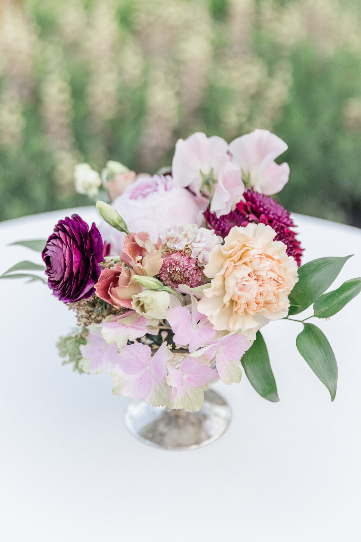 A wedding centerpiece  with  peach, lavender, and pops of dark purple