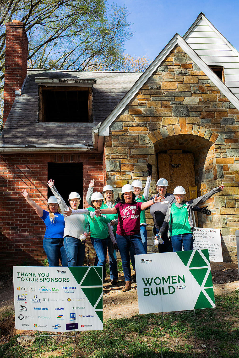 Group of people in hard hats posing in front of a brick building.