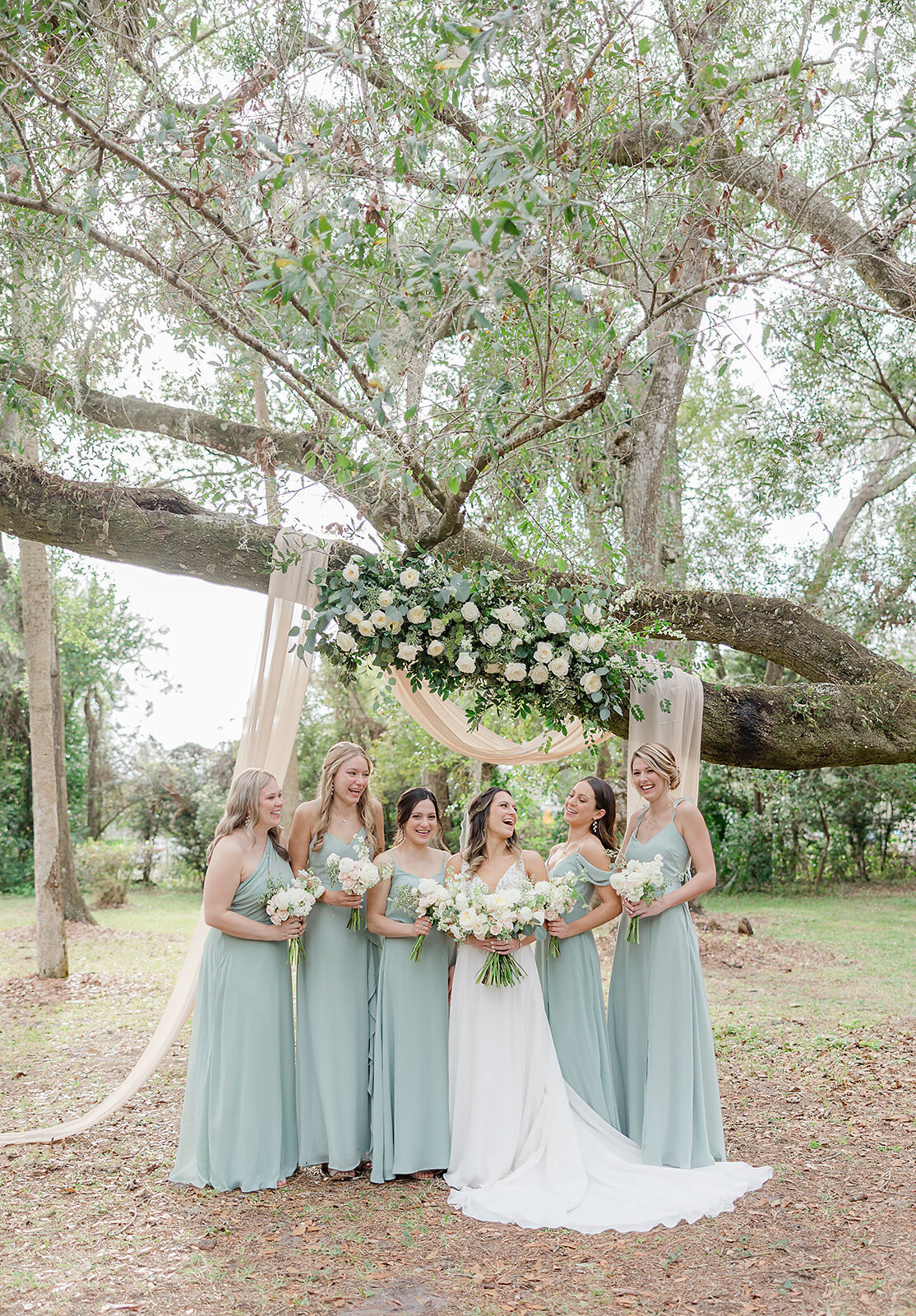 Bride laughing with bridesmaids under a tree at Gardenvilla in Winter Park Florida 