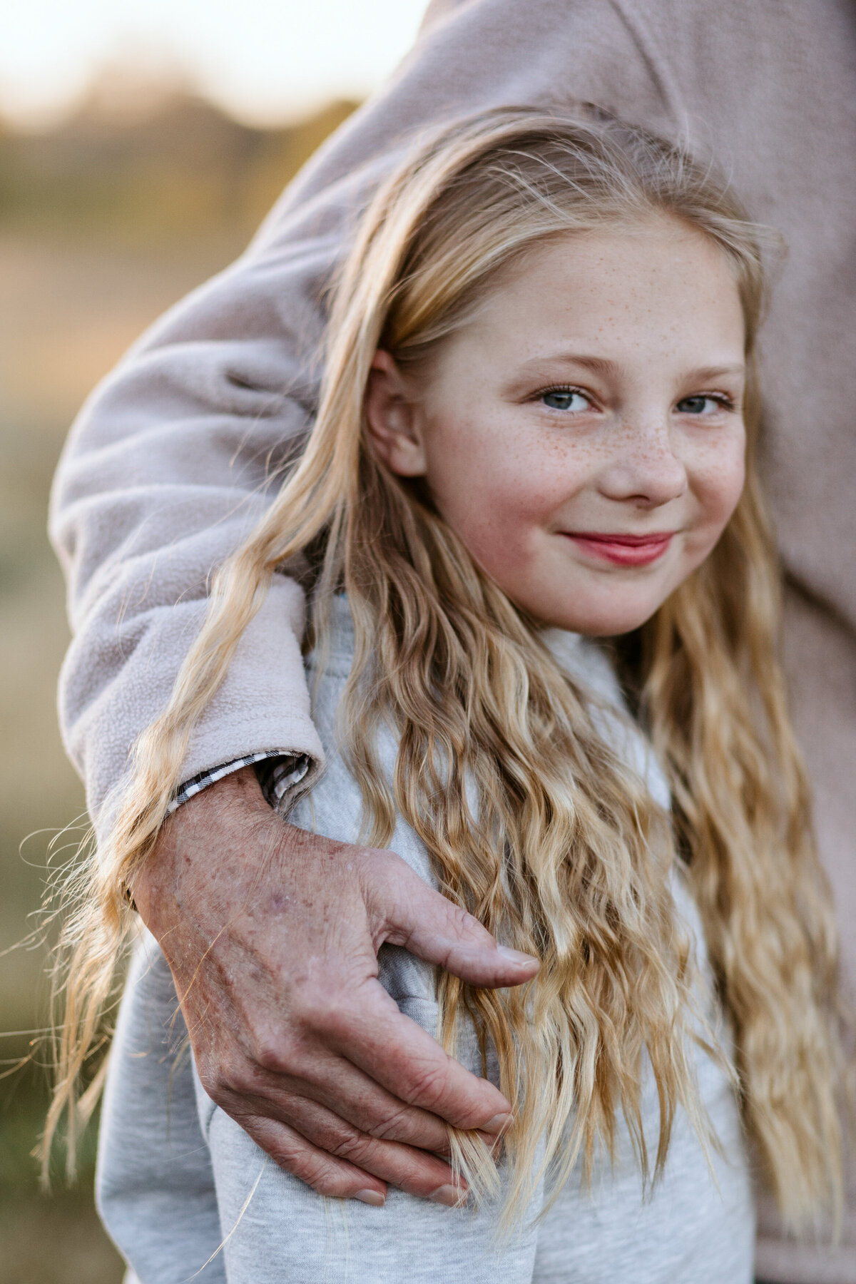 Grandmother wraps her arms around her teenage granddaughter with long blonde hair in a warm embrace